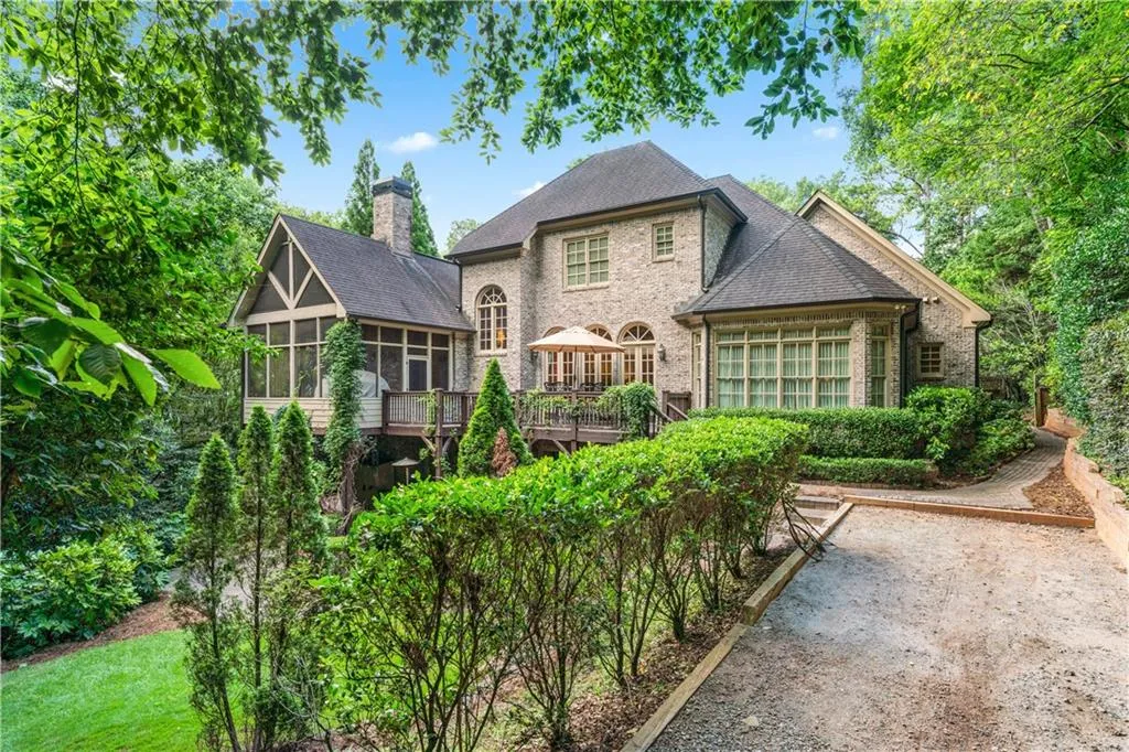 Back of property with a sunroom, a chimney, brick siding, a wooden deck, and a shingled roof