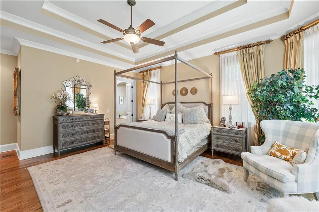 Bedroom featuring a tray ceiling, crown molding, wood finished floors, and multiple windows