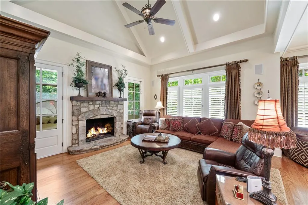 Living room featuring high vaulted ceiling, light wood finished floors, a stone fireplace, ceiling fan, and beam ceiling