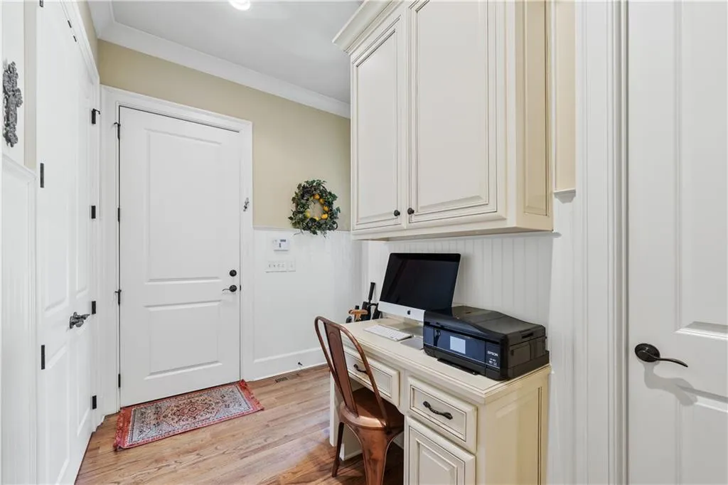 Office with light wood finished floors, ornamental molding, and a wainscoted wall