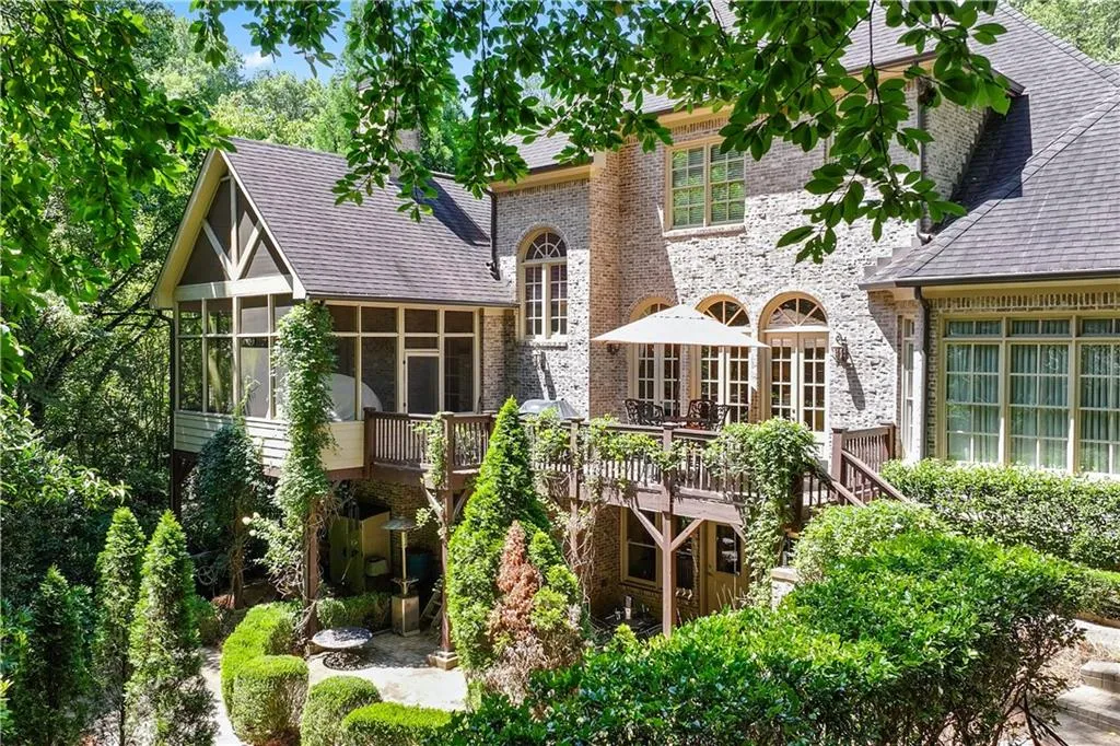 Back of property featuring a sunroom, a shingled roof, a wooden deck, and brick siding