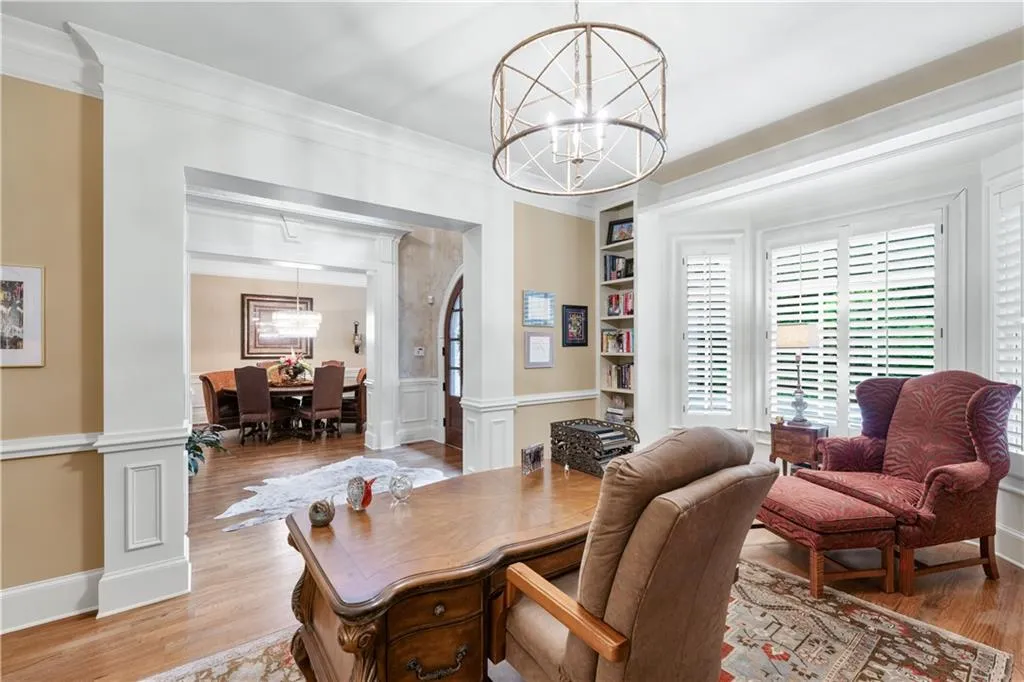 Home office featuring a chandelier, light wood-style floors, ornamental molding, wainscoting, and a decorative wall
