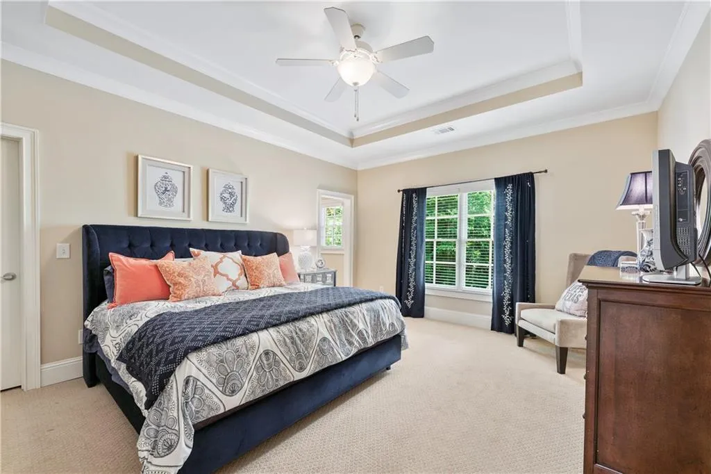 Carpeted bedroom with a raised ceiling, ornamental molding, and a ceiling fan