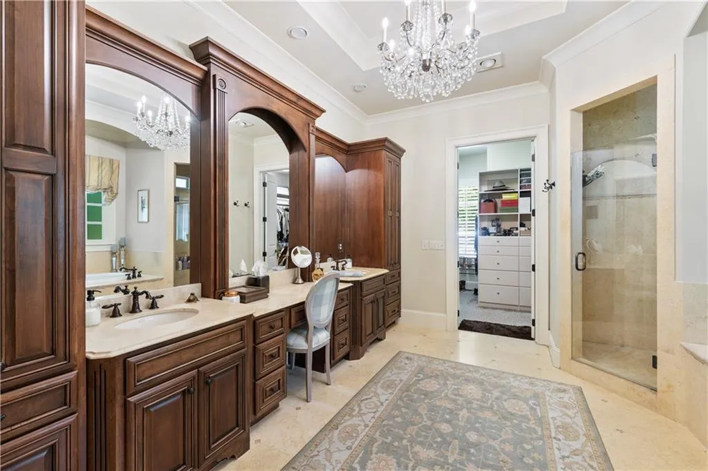 Bathroom featuring a chandelier, crown molding, double vanity, a stall shower, and a spacious closet