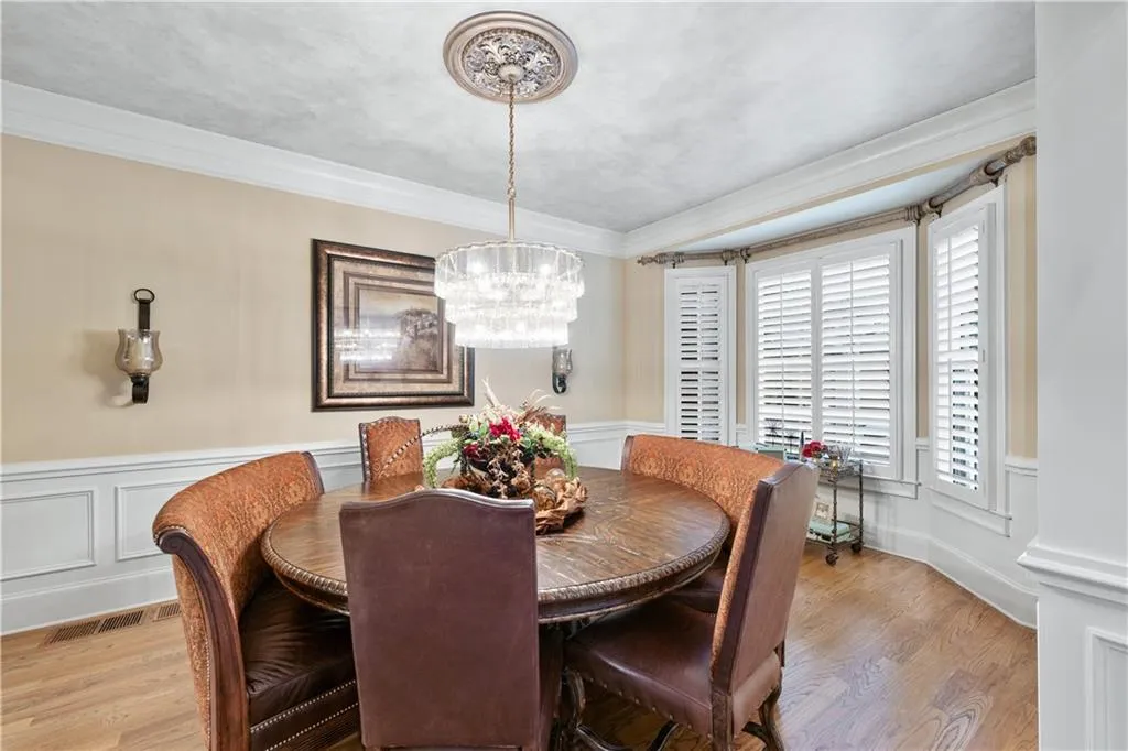 Dining area with light wood finished floors, a chandelier, ornamental molding, a wainscoted wall, and a decorative wall
