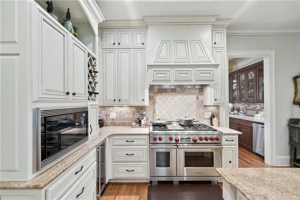 Kitchen with appliances with stainless steel finishes, ornamental molding, light stone countertops, backsplash, and light wood finished floors
