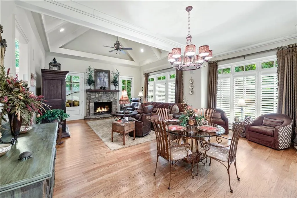 Dining area with healthy amount of natural light, a chandelier, light wood-type flooring, a stone fireplace, and beam ceiling