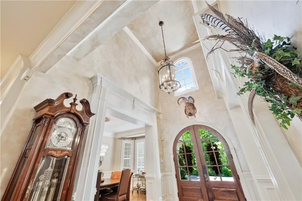 Entrance foyer with a high ceiling, french doors, plenty of natural light, a chandelier, and a wainscoted wall