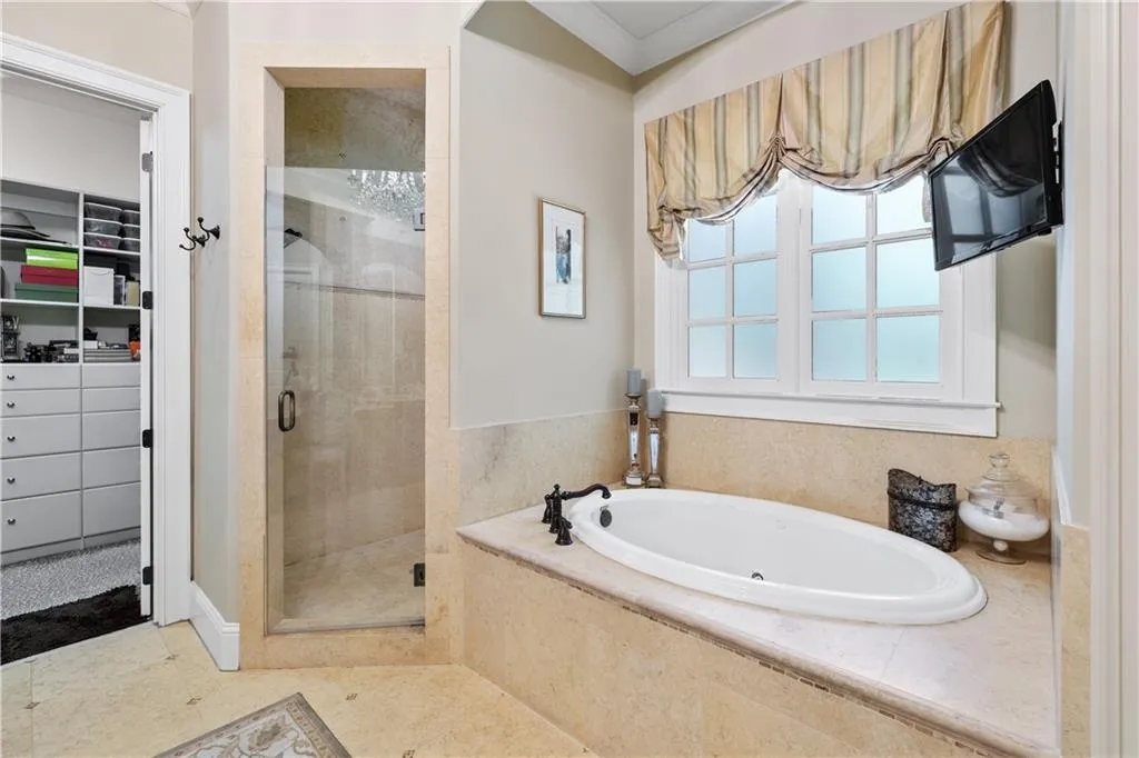 Full bathroom featuring a shower stall, a garden tub, a spacious closet, and crown molding