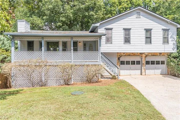 Split-level residence featuring a covered front porch with lattice railing, a two-car garage with stone accents, a gabled roofline, and an exterior staircase