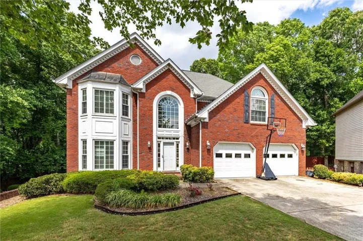 Brick exterior residence featuring a prominent arched window, a two-car garage, a bay window, and a manicured front lawn with established landscaping