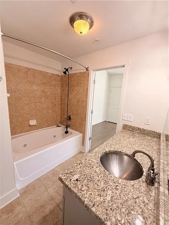 Jetted tub with tile surround, vanity with stone countertop, undermount sink, and tiled flooring