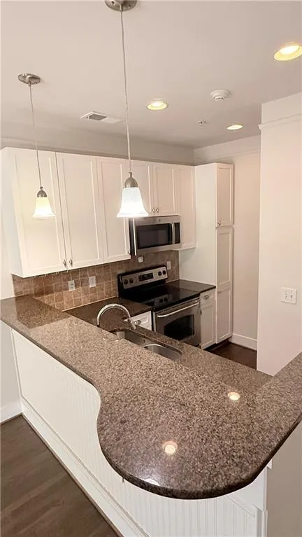Kitchen featuring a curved breakfast bar, stone countertops, white shaker-style cabinetry, and stainless steel appliances