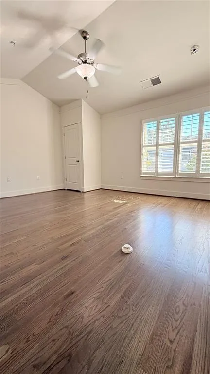 Vaulted ceiling with a ceiling fan light fixture, wood-finish flooring, and window shutters