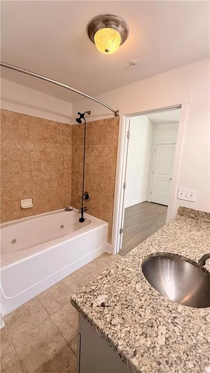 Bathroom featuring a jetted tub with tiled surround, a vanity with a granite-style countertop, and a stainless steel undermount sink