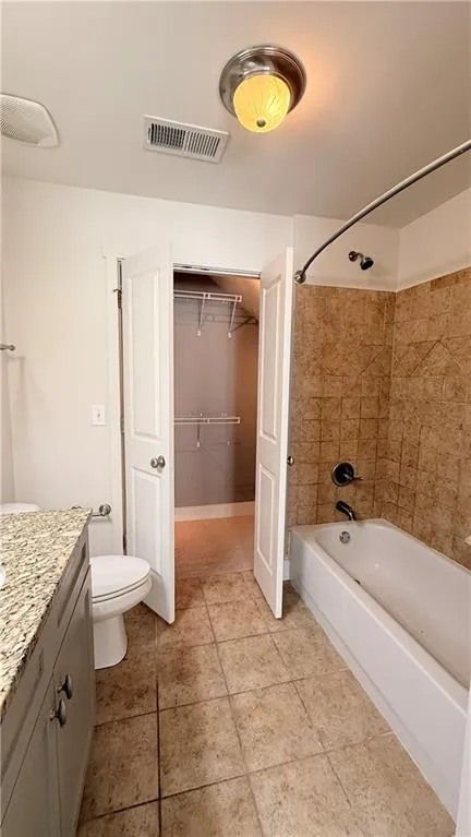 Bathroom featuring a bathtub with tiled surround, a toilet, and a vanity with a stone-finish countertop