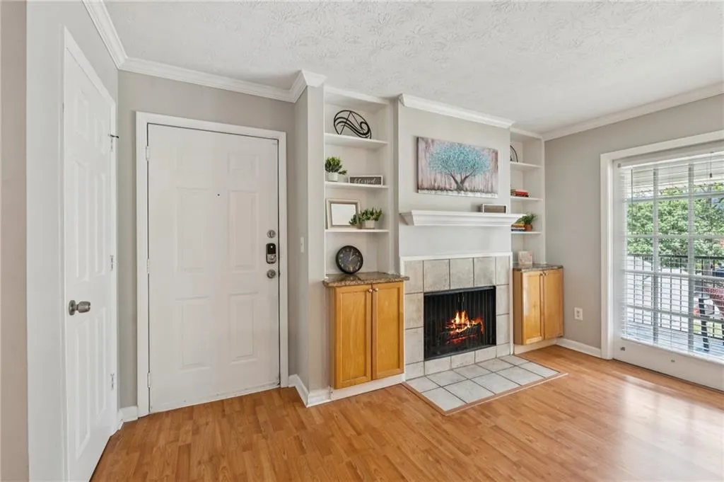 Unfurnished living room with built in features, a tile fireplace, light wood finished floors, ornamental molding, and a textured ceiling