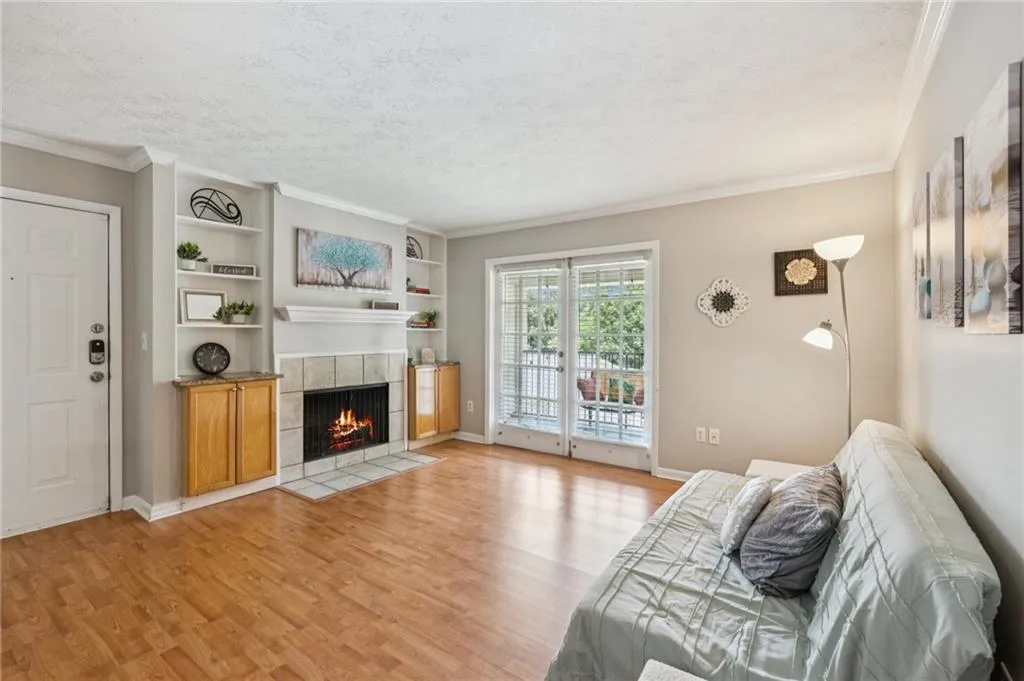 Living area featuring a tile fireplace, crown molding, light wood-style floors, built in shelves, and a textured ceiling
