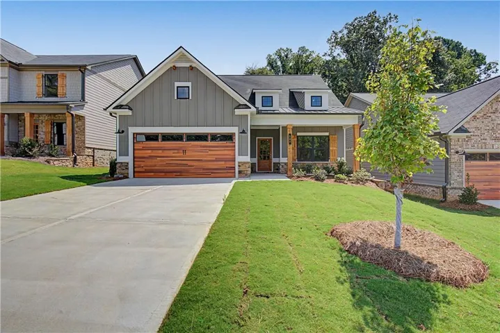 Craftsman-style home featuring a wood-panel garage door, dormer windows, covered front porch with wood columns, and concrete driveway