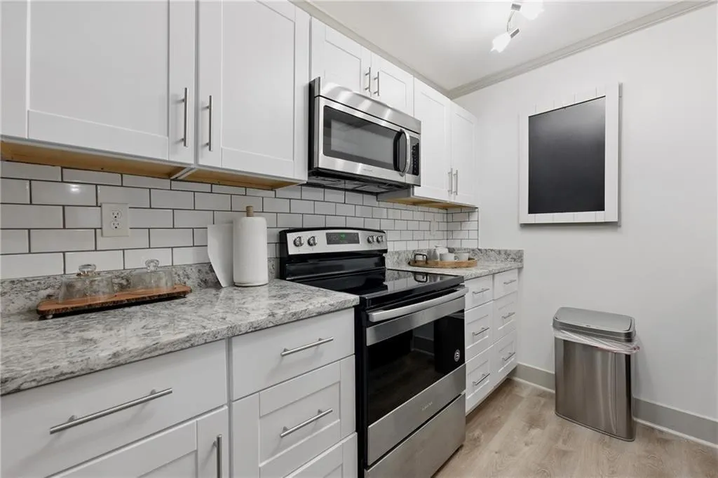 Kitchen with stainless steel appliances, white cabinets, backsplash, light wood-style flooring, and ornamental molding Kitchen with stainless steel appliances, white cabinets, backsplash, light wood-style flooring, and ornamental molding
