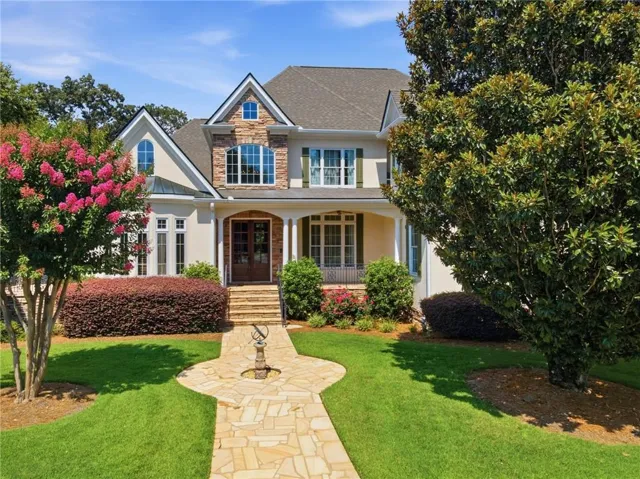 Stucco and stone exterior featuring multiple gables, a covered entry porch, an arched front door, and a flagstone walkway