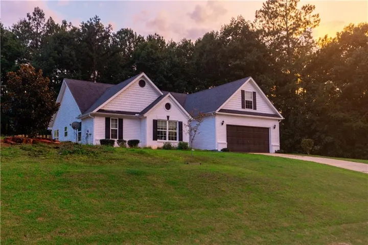 Single-story residence featuring white siding, a two-car garage with a dark wood-finish door, and a paved driveway