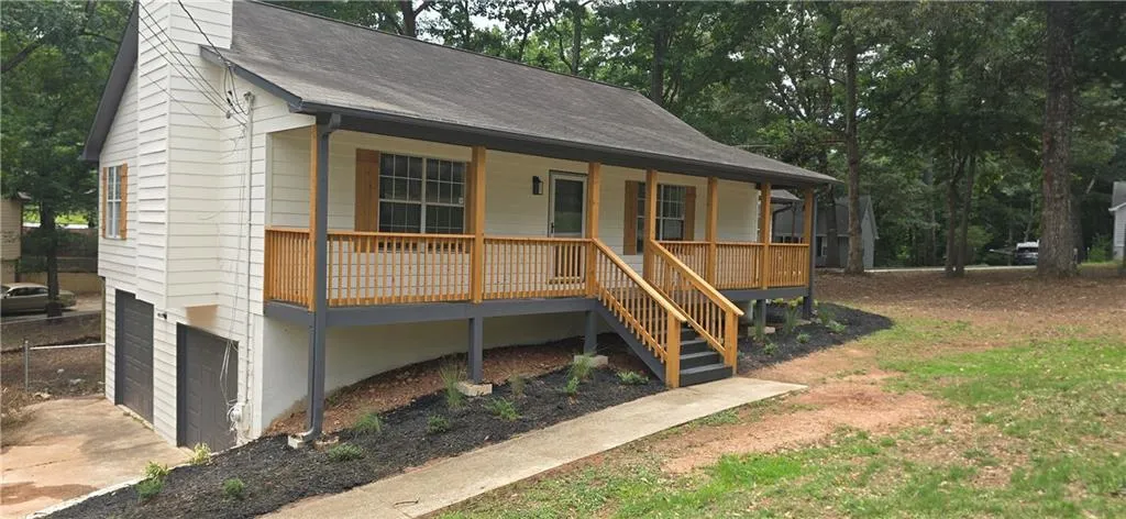 Front elevation featuring a full-width porch with natural wood railings, exterior siding, a two-car garage, and a landscaped front garden bed