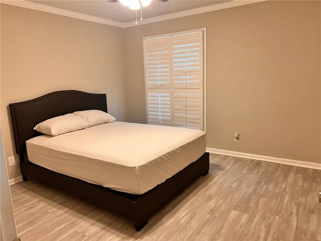 Bedroom featuring light wood finished floors, crown molding, and a ceiling fan