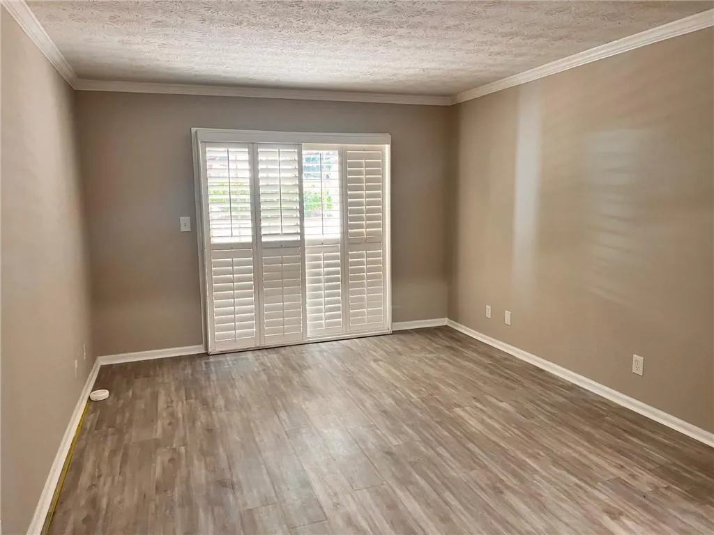 Empty room with crown molding, a textured ceiling, and light wood-style floors
