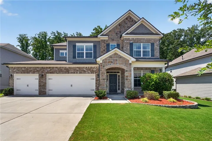 Brick and stone facade, two-car garage, covered porch entry, well-maintained lawn, and established landscaping