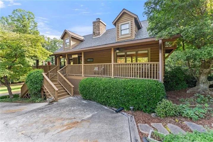 Wood-sided home with a prominent stone chimney, multi-level wooden deck, and a dormer window