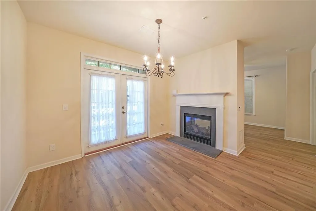 Unfurnished living room with light wood-style floors, a glass covered fireplace, french doors, and a chandelier