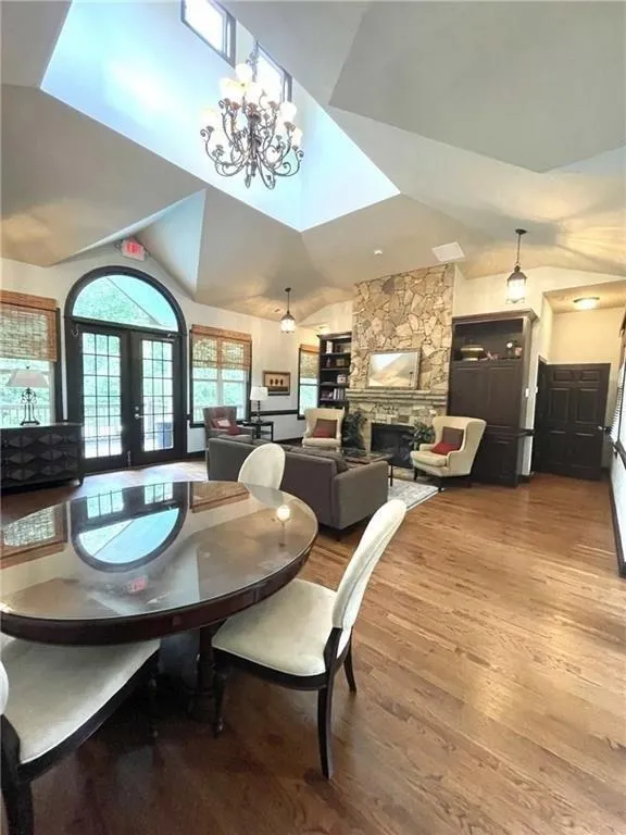 Dining room featuring french doors, wood finished floors, a stone fireplace, a chandelier, and high vaulted ceiling
