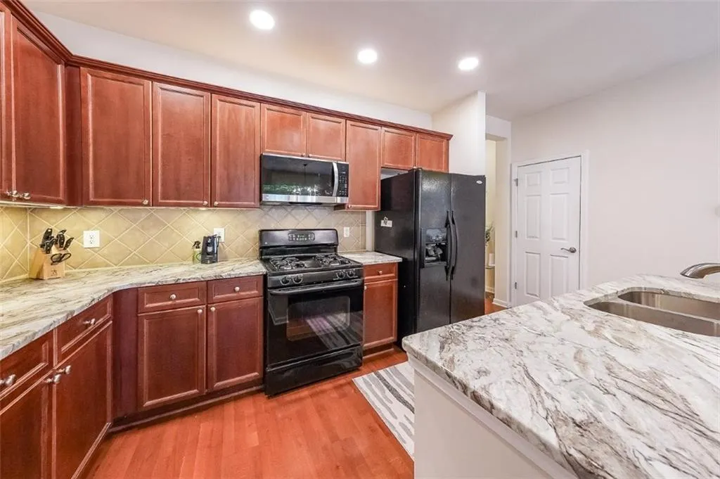 Kitchen featuring black appliances, tasteful backsplash, light wood-style flooring, light stone counters, and recessed lighting