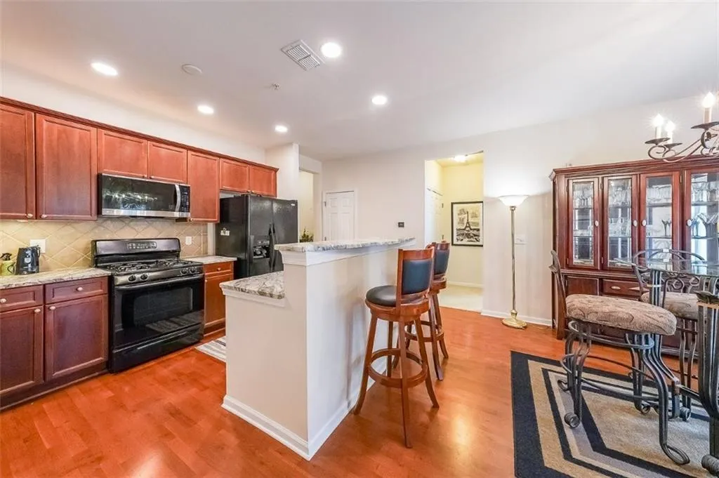 Kitchen featuring black appliances, backsplash, a kitchen breakfast bar, light stone countertops, and recessed lighting