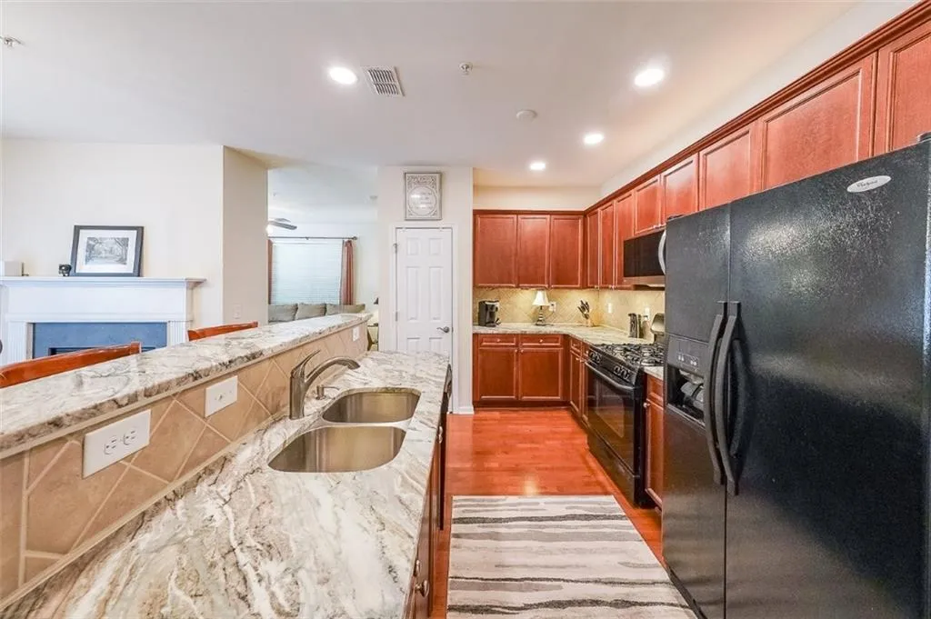 Kitchen with black appliances, light wood-type flooring, decorative backsplash, light stone counters, and recessed lighting