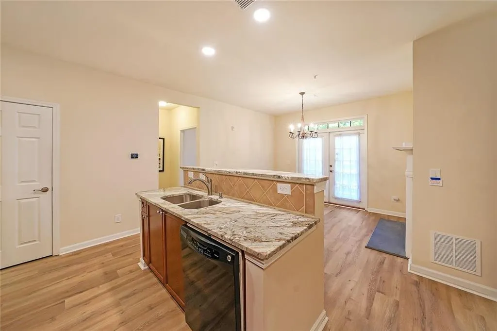 Kitchen with decorative light fixtures, a center island with sink, black dishwasher, light stone countertops, and light wood-type flooring