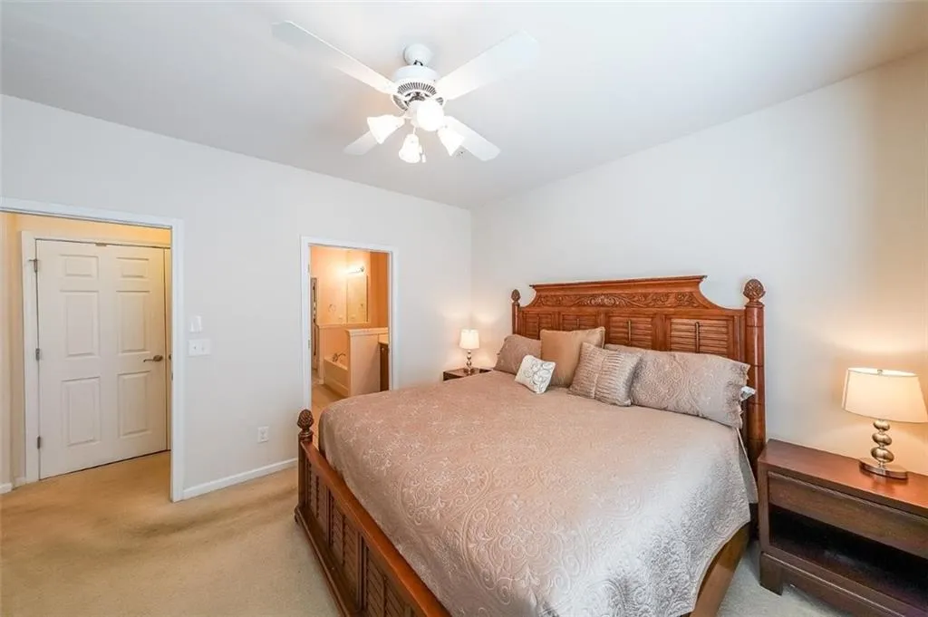 Bedroom featuring ensuite bath, light colored carpet, and ceiling fan