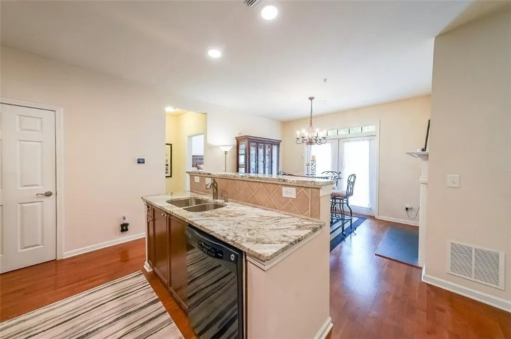 Kitchen featuring light stone countertops, black dishwasher, decorative light fixtures, a chandelier, and dark wood-style floors
