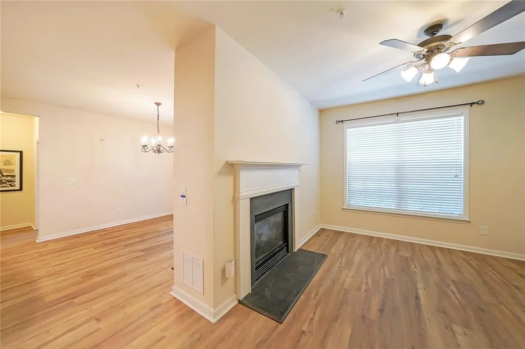 Unfurnished living room with light wood finished floors, a glass covered fireplace, ceiling fan, and a chandelier