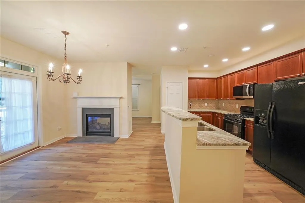 Kitchen featuring black appliances, light wood-style flooring, a center island with sink, a glass covered fireplace, and recessed lighting