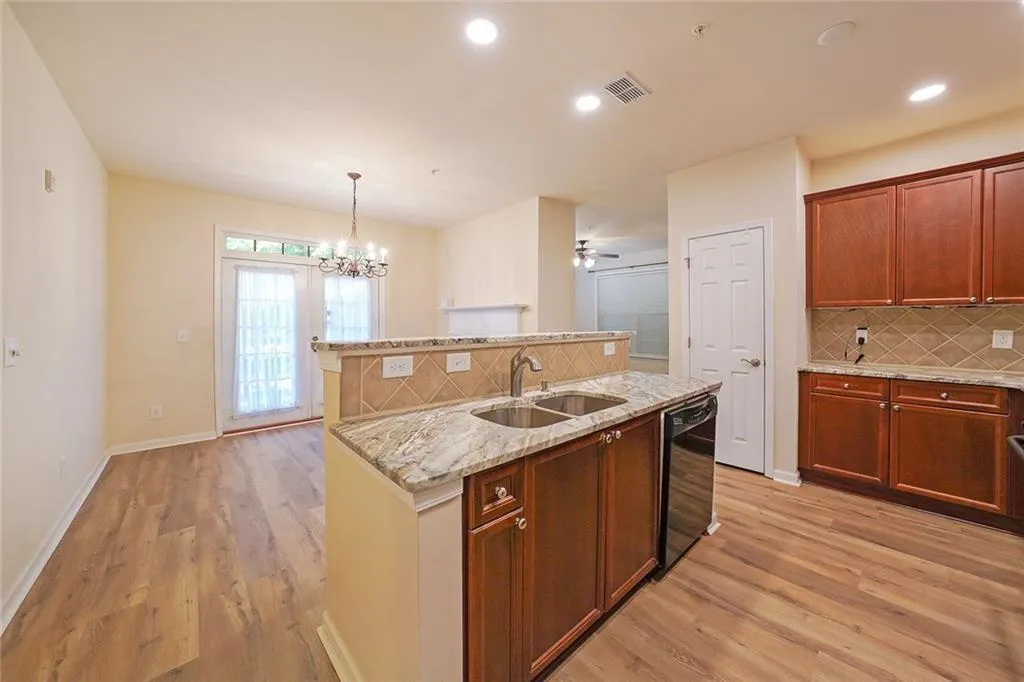 Kitchen with backsplash, hanging light fixtures, an island with sink, light stone counters, and light wood-style floors