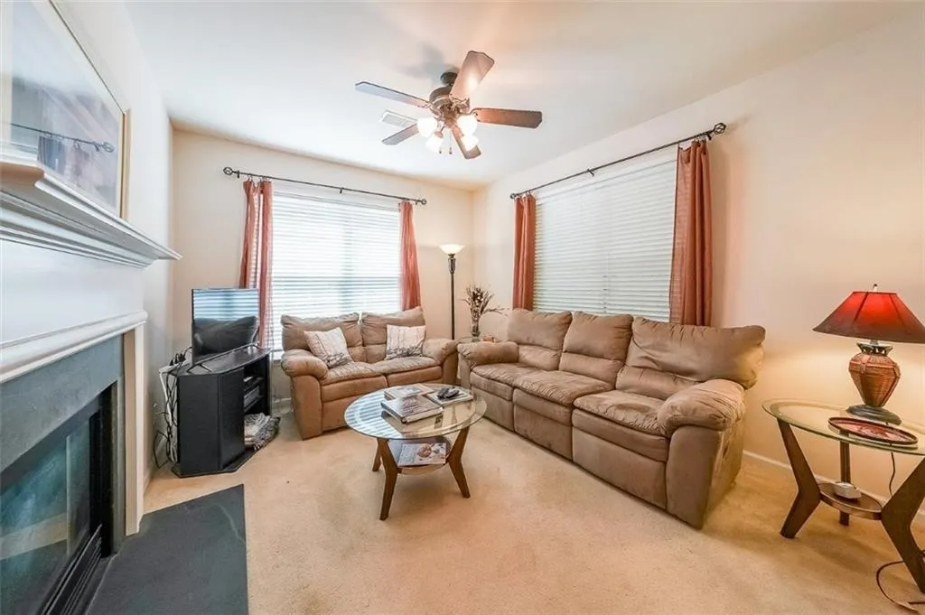 Carpeted living area featuring a fireplace with flush hearth and ceiling fan