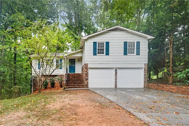 Split-level residence featuring white siding, brick accents, blue shutters, and a two-car garage