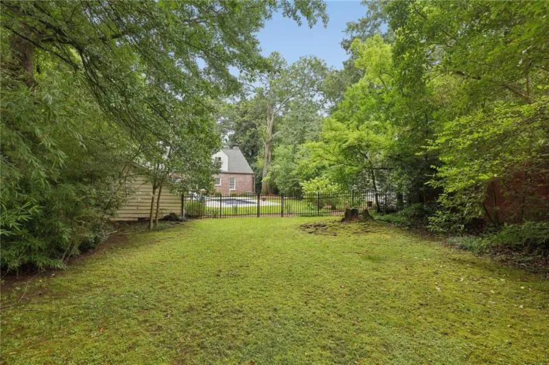 Expansive lawn with mature trees and a black metal fence, featuring a wood-sided outbuilding