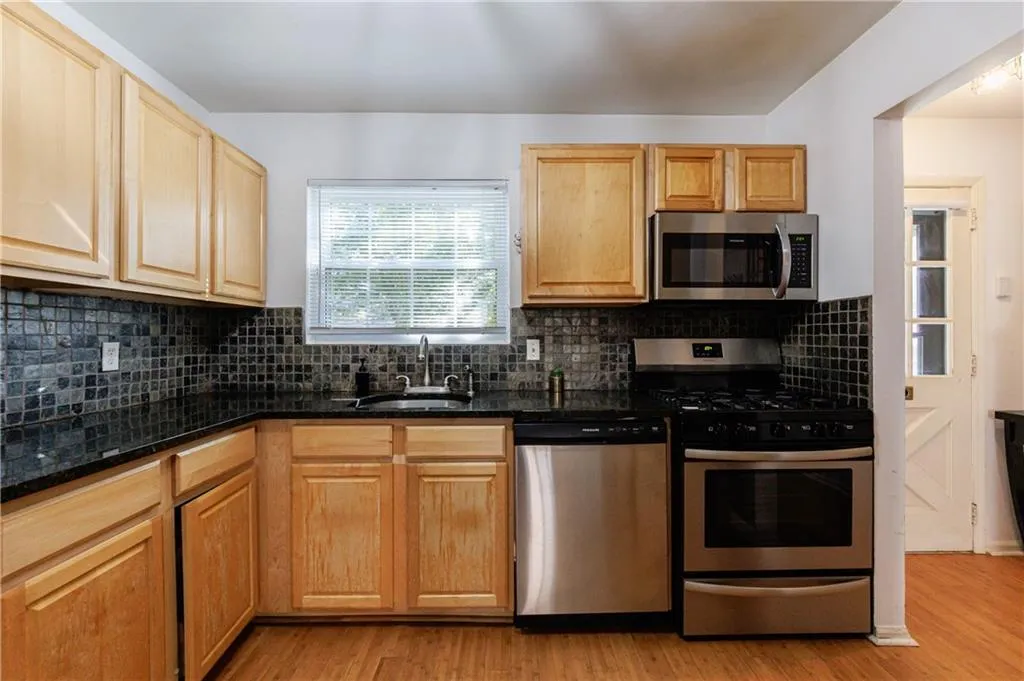 Kitchen with appliances with stainless steel finishes, light wood-type flooring, decorative backsplash, and dark stone countertops