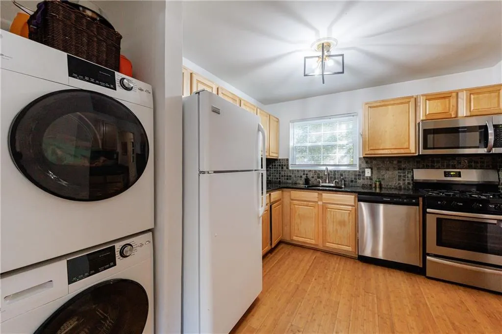 Kitchen with stainless steel appliances, light wood finished floors, backsplash, stacked washing machine and dryer, and light brown cabinets