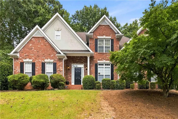 Brick facade with stucco gables, black window shutters, white trim, and a prominent front entry with a dark door
