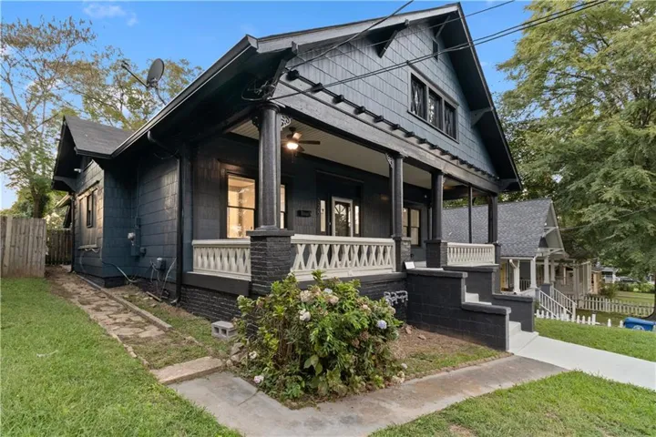 Exterior featuring dark siding, a covered porch with decorative railing, and an architectural shingle roof