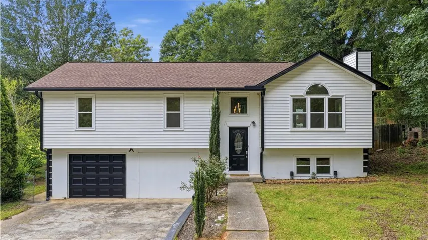 White siding exterior with a brown shingle roof, integrated garage, and a black front door